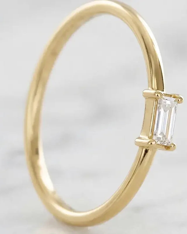 Solitaire baguette diamond engagement ring in 18K yellow gold by Mayuri, on an elegant background