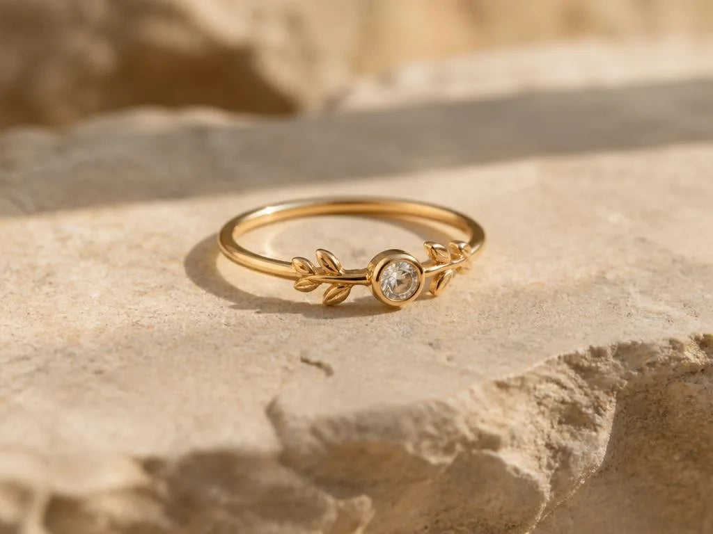 A delicate 18K yellow gold ring featuring a diamond and leaf motif, resting on a natural stone surface, a romantic design by Mayuri