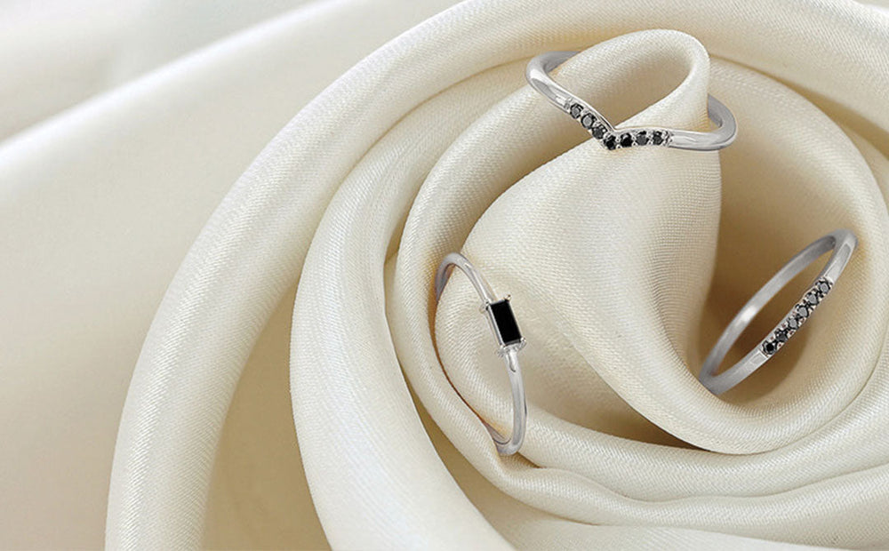 Delicate white gold rings set with black diamonds, resting on an ivory satin fabric for jewellery care