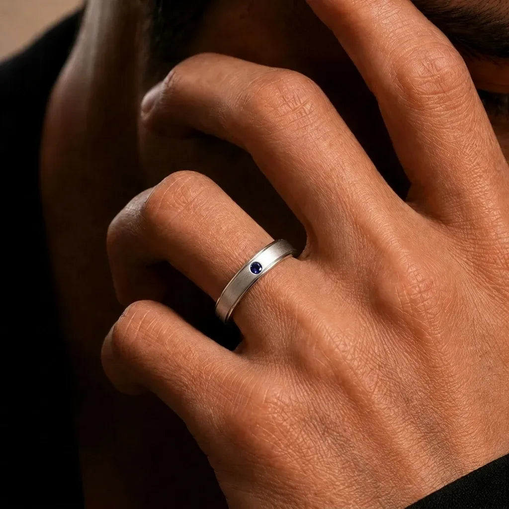 18K white gold band ring set with a blue sapphire, worn on the finger, by Mayuri