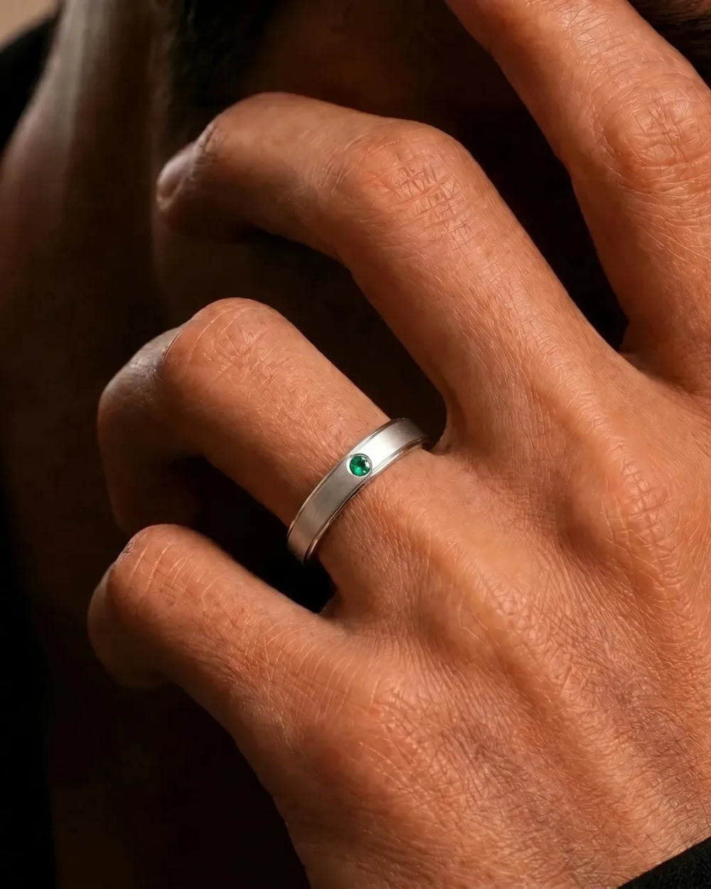 18K white gold band ring set with an emerald, worn on the finger, by Mayuri