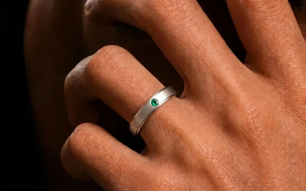 18K white gold band ring set with an emerald, worn on the finger, by Mayuri