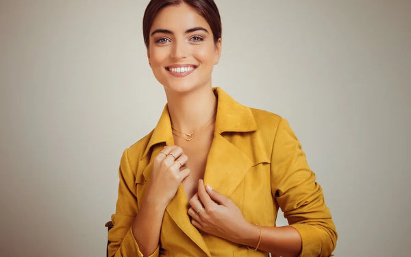 Yellow gold rings and bracelet worn by a woman in an ochre jacket on a beige background, Mayuri