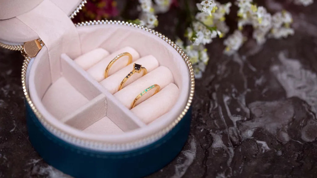 Round jewellery box with separate compartments holding three rings in yellow gold, ruby, and emerald