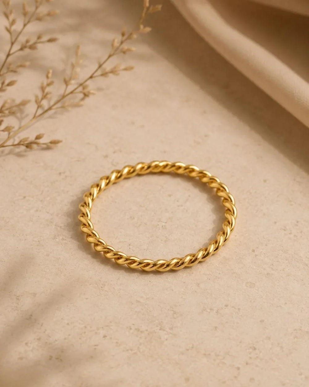 Twisted Musubi wedding ring in 18K yellow gold on a natural beige background, by Mayuri