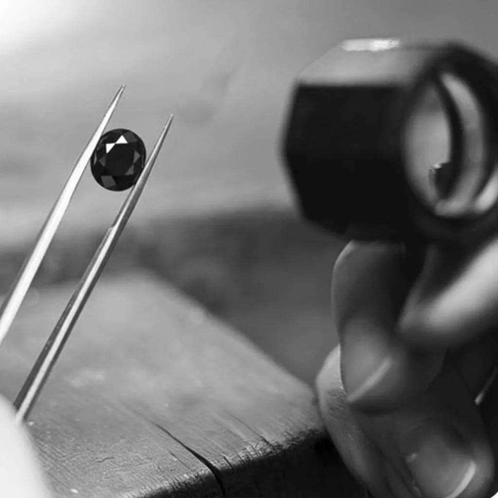 Cut black diamond held by gemologist tweezers with an inspection loupe in the background