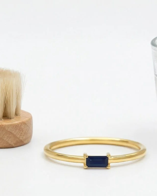 18K yellow gold ring set with a baguette-cut sapphire, shown with a soft brush and a glass of lukewarm water