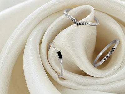 Delicate white gold rings set with black diamonds, resting on an ivory satin fabric for jewellery care