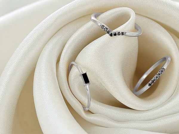 Delicate white gold rings set with black diamonds, resting on an ivory satin fabric for jewellery care