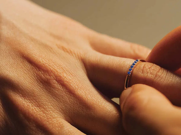 18K rose gold wedding ring set with blue sapphires, worn on a hand, jewellery care