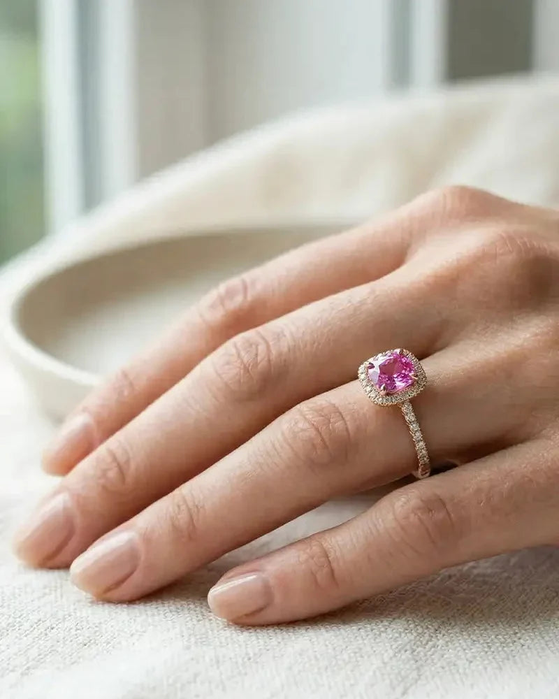 Pink sapphire engagement ring with diamond halo, set in 18K rose gold, worn on the hand