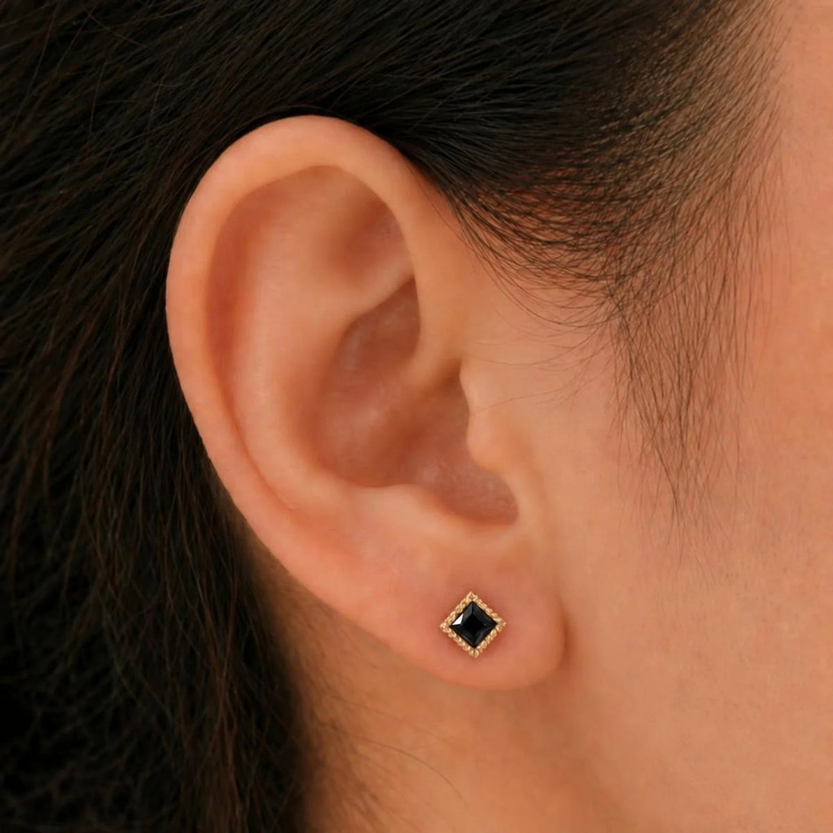 Indrani black diamond earrings worn on the ear, princess-cut stud in twisted rope setting, yellow gold