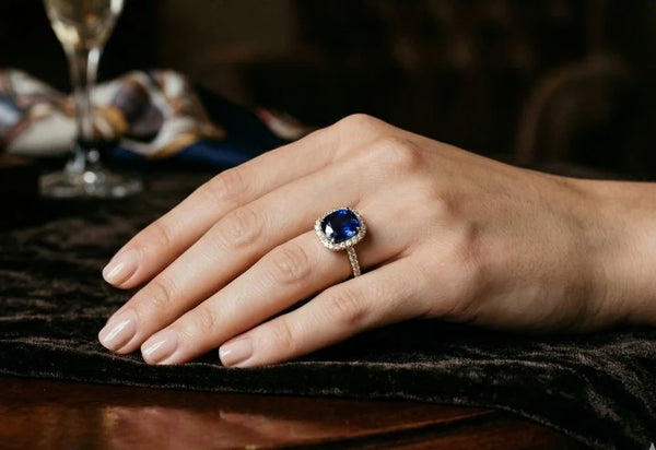 Deep blue cushion-cut sapphire ring surrounded by diamonds, worn on the ring finger
