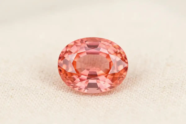 Oval-cut padparadscha sapphire, a rare pink-orange gemstone with brilliant multifaceted reflections