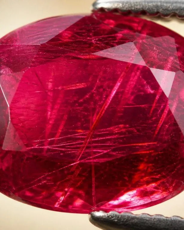 Natural ruby held in gemological tweezers, revealing visible rutile inclusions within