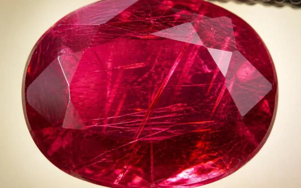 Natural ruby held in gemological tweezers, revealing visible rutile inclusions within